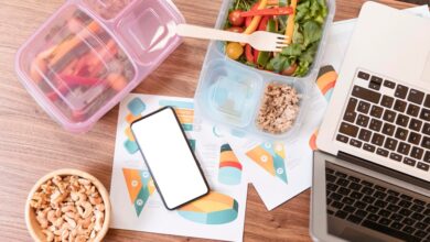 a lunch box with vegetables and a phone next to a laptop